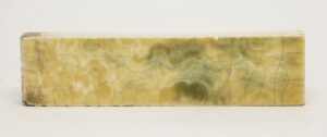 Single yellow crackled ceramic tile with a glossy glaze, visible age-related chips, and greenish mottling across the surface.