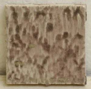 Single antique square ceramic wall tile with a pale mottled purple crackled surface and visible age-related chips and scrapes.