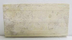 Tan ceramic tile with visible age-related imperfections and minor chips shown in a close-up.
