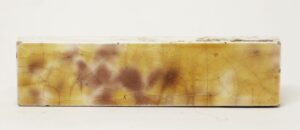 Single yellow crackled ceramic tile with a shiny glaze and visible age-related chips along the edges.