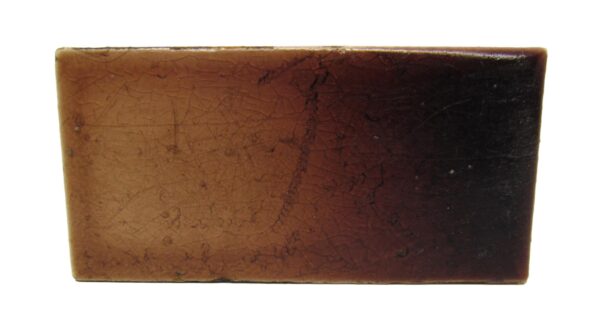 Single brown ceramic tile with a light-to-dark gradient and visible age-related surface wear.