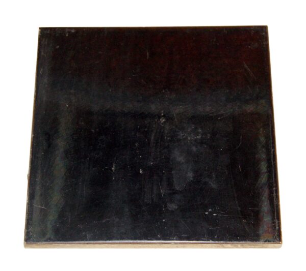 Vintage black square wall tile with a shiny surface and visible age-related scratches and minor edge wear.