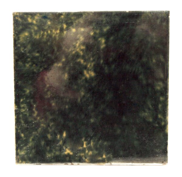 Dark green ceramic wall tile shown front on, with visible age-related imperfections and minor chips along the edges.