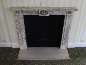Front view of a marble mantel with gray veining, carved channels, and round cameo medallions at the upper corners.