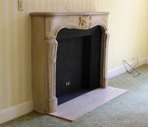 Louis XV carved limestone mantel with a replacement hearth shown installed, featuring an ornate arched opening and decorative central crest.