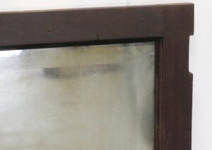 Close-up of a cabinet door mirror with a dark wood tone frame and beveled glass edge, showing the upper right corner and distressed surface details.