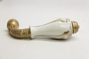 Ornate faucet handle with a white porcelain grip and antique brass details shown in profile.