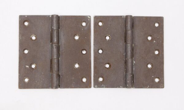 Pair of vintage cast iron butt door hinges shown side by side, each with five knuckles, a staggered hole pattern, and visible surface wear from prior use.