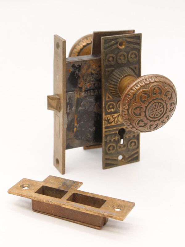 Antique bronze passage door knob set with ornate round knob, rectangular back plate, mortise lock, and strike plate shown separated on a white background.