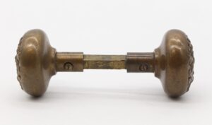 Pair of antique bronze entry door knobs with a square spindle and four-fold Flemish design, shown in profile.