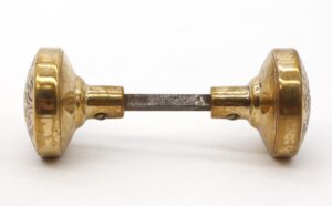 Pair of bronze door knobs with a spindle, shown in side view with aged polished finish and visible wear.