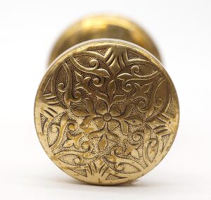 A round bronze door knob with an ornate fourfold pattern and visible age wear is shown in close-up front view.