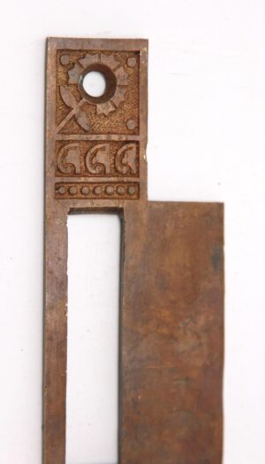 Ornate brass strike plate cover with a rectangular cutout and decorative geometric engraving at the top.