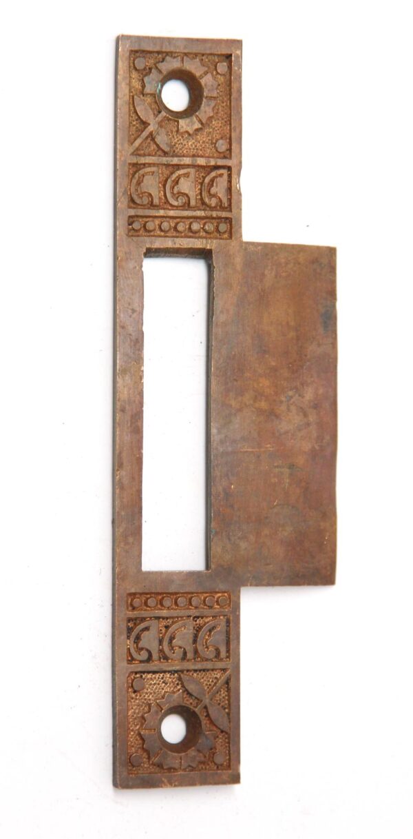 Ornate brass strike plate cover with an elongated rectangular opening and decorative geometric engraving at both ends.