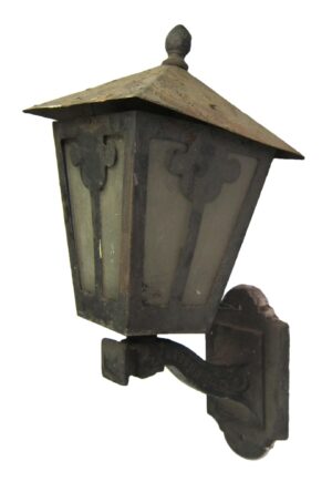 Arts and Crafts wrought iron exterior wall sconce with a peaked top, glass panels, and a mounting bracket.