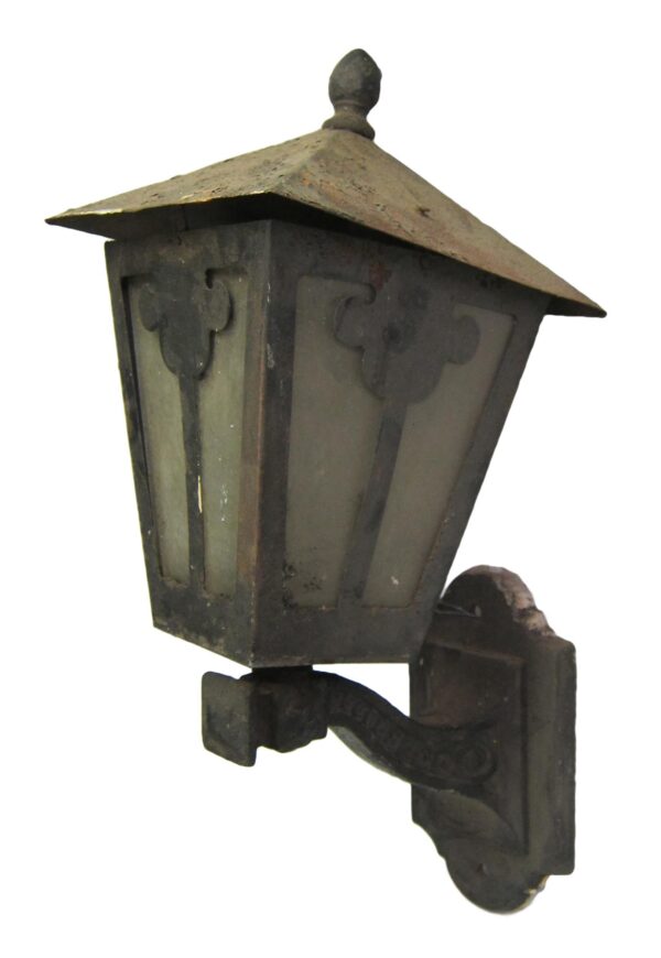 Arts and Crafts wrought iron exterior wall sconce with a peaked top, glass panels, and a mounting bracket.