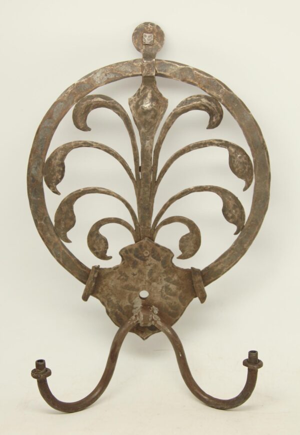 Arts and Crafts cast iron sconce with a circular scrollwork frame and two curved hooks below.