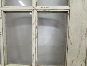 Vintage white wood door with divided glass panes, shown in close-up with one broken pane.