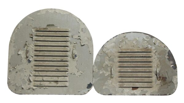 Pair of arched cast iron grates shown as a set, one painted gray and the other white, both with worn louvered slats and peeling paint.