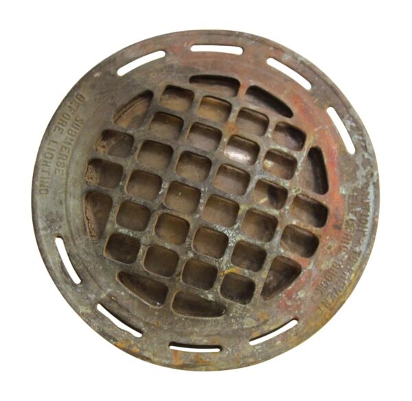 Close-up of a round bronze submersible light with a perforated grid face and slotted rim openings, shown from above.