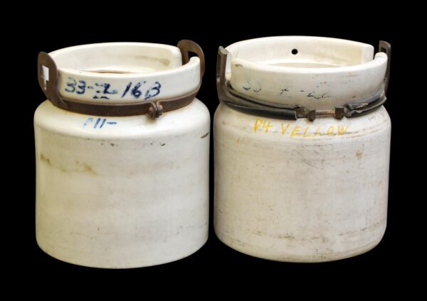 Pair of white ceramic jugs with porcelain finish, shown side by side with metal handles and visible age marks and handwritten numbers.