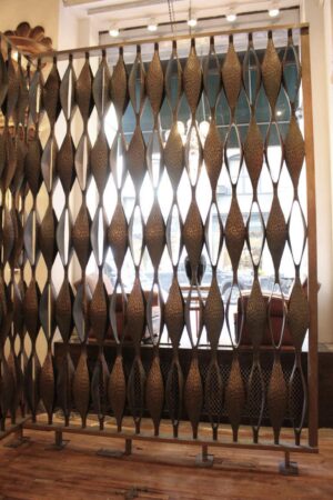 A metal Mid Century Modern room divider features diamond designs and textured gold accents on a wooden floor, set in a bright, spacious interior for both function and stylish visual interest.