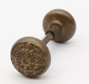 Pair of antique bronze entry door knobs shown connected by a spindle, with one knob facing forward and the other angled behind it.