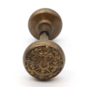 Antique bronze entry door knob with a Flemish four fold floral rosette and part of the spindle visible.