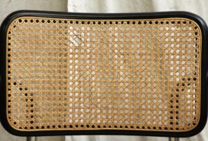 Close-up of a mid century cane chair seat with a black frame and tan woven wicker panel.