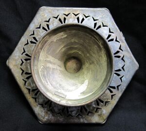 Hexagon serving dish with a pedestal bowl and floral cutout rim, shown from above with visible wear on the aluminum surface.