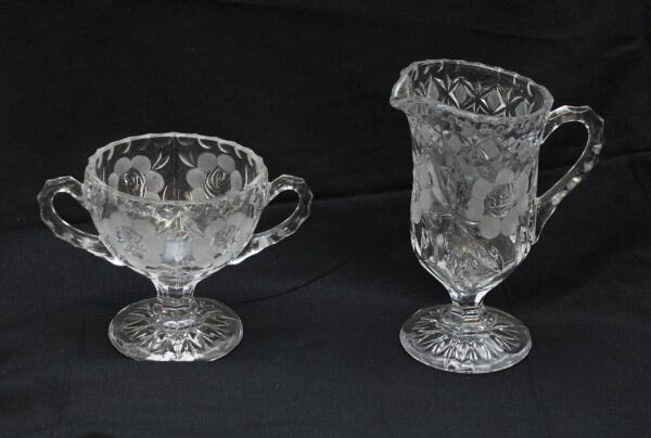 Pair of clear glass creamers and dessert bowls with floral etching, shown as a matching pair with handles and pedestal bases.