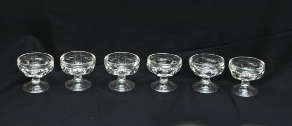 Six clear glass dessert bowls with short pedestal bases are shown in a row as a set.