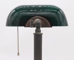 Desk lamp with a green and white glass shade, fluted brass base, and pull chain switch.