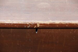 Close-up of a dark wood cedar chest showing worn top edges and a center keyhole opening.