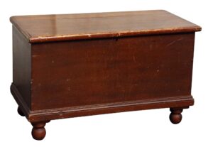 Dark wood cedar chest with a worn top, front panel, and turned feet, shown in a three-quarter view.