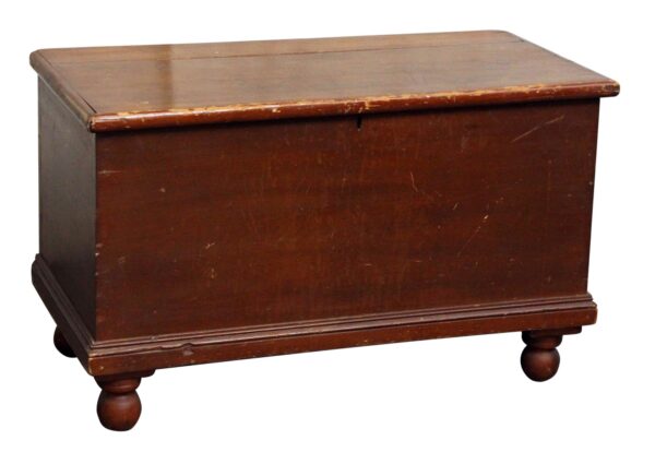 Dark wood cedar chest with a worn top, front panel, and turned feet, shown in a three-quarter view.