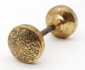 Pair of ornate bronze door knobs with a spindle, one knob showing a detailed four-fold pattern.