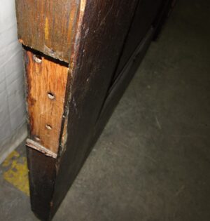Close-up of a dark wood interior door edge showing the latch side and worn vertical stiles.