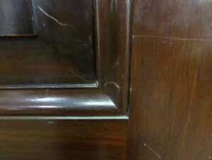 Close-up of a two-panel door in dark wood tone with visible chips along the bottom edge and frame.