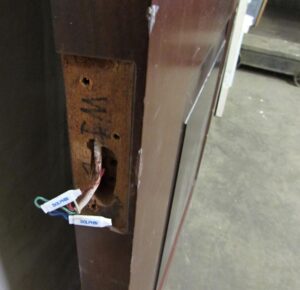 Close-up of the door edge showing a recessed hardware opening and exposed wires on a dark wood tone two-panel door.