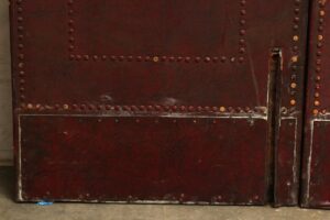 Red leather-studded door panel with vertical and horizontal rows of studs and a narrow latch opening on the right side.