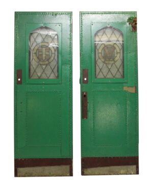 Pair of antique single-panel doors shown front and back, with green painted faces, arched stained glass windows, studded edges, and visible wear near the hardware and lower panels.