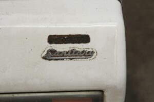 Close-up of a white metal sanitary scale with a Sanitary badge and a worn rectangular label above it.
