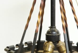 Close-up of a gothic pendant light with black and copper finish, showing the central stem, twisted metal accents, and bulb holders, with the bottom glass missing.