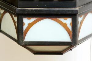 Close-up of a Gothic pendant light showing the black and copper frame and frosted glass panels, with the bottom glass panel missing.