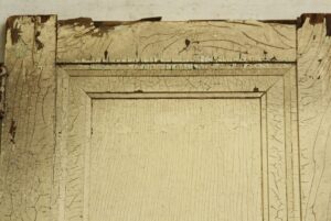 Close-up of a white wood door with one raised panel and heavily cracked painted finish, showing the upper section and side stiles.