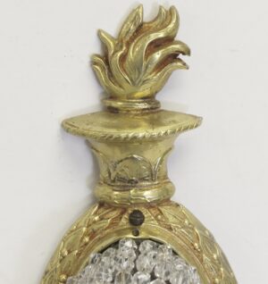 Close-up of a restored French wall sconce in gilt bronze with a clear crystal beaded section and ornate leaf detail at the top.