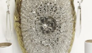 Close-up of a restored French wall sconce with clear beaded crystal detail and a central floral rosette on a gilt bronze frame.