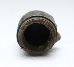 Front view of a small round cast iron mold with a hollow opening and worn, rusted edges.