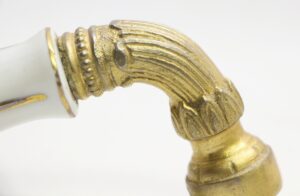 Close-up of an ornate faucet handle with a white porcelain grip and an antique brass curved lever.